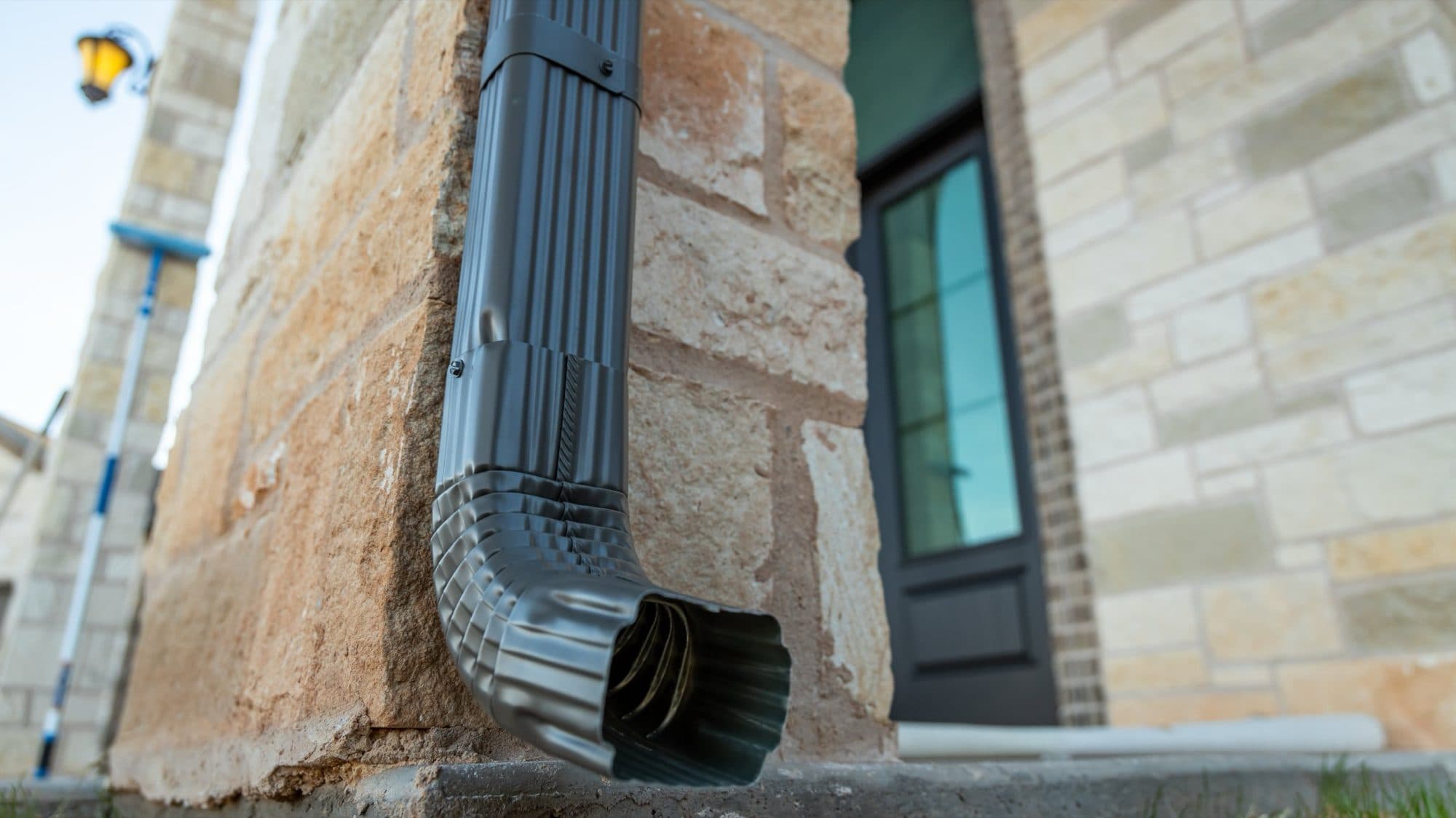Downspout and elbow installed against a stone wall
