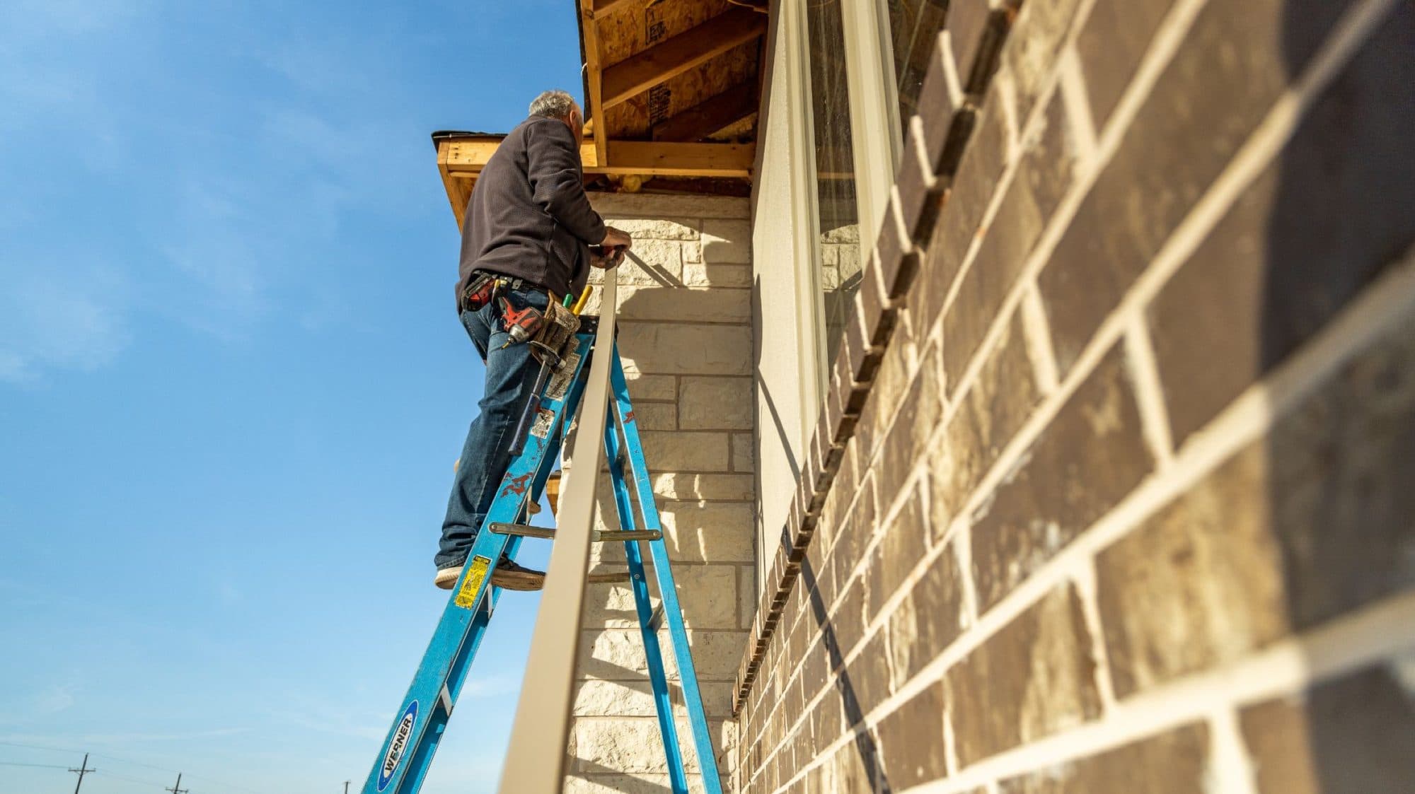 Installer working from a ladder at the roof edge of a home